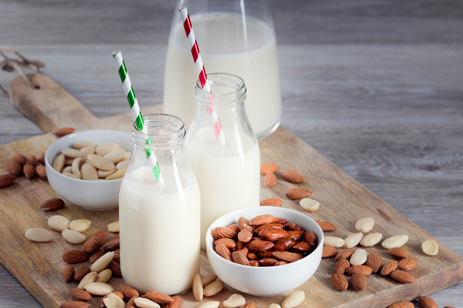 Mood picture "alcohol-free almond cocktail": two filled wide-neck bottles with colorful straws stand on a wooden board with almonds